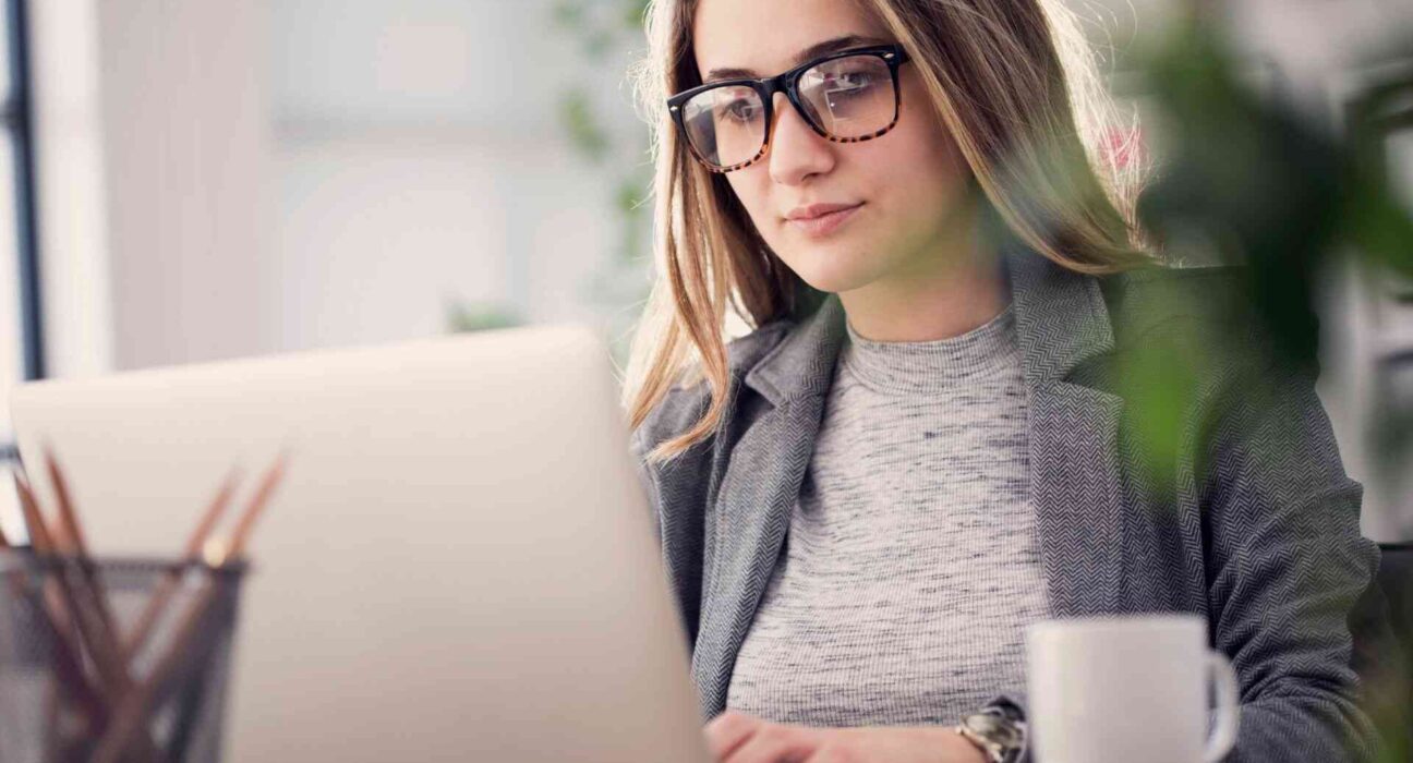 Kobieta w okularach pracuje przy laptopie w biurze, planując promocję sklepu internetowego.