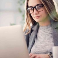 Kobieta w okularach pracuje przy laptopie w biurze, planując promocję sklepu internetowego.