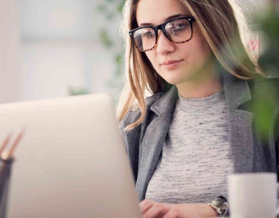 Kobieta w okularach pracuje przy laptopie w biurze, planując promocję sklepu internetowego.