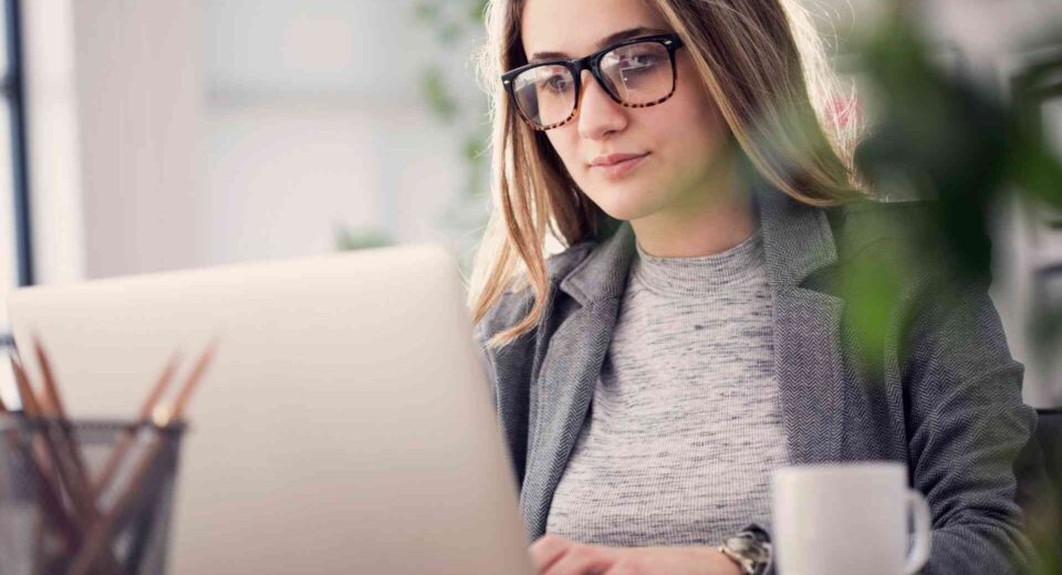 Kobieta w okularach pracuje przy laptopie w biurze, planując promocję sklepu internetowego.